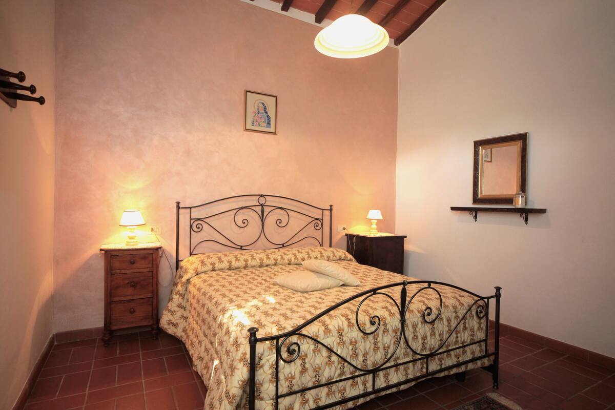 Ein Schlafzimmer mit einem Bett, zwei Nachttischen mit Lampen, einem Wandregal und einem gerahmten Bild über dem Bett.