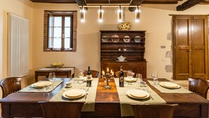 Een eetzaal met een houten tafel gedekt voor zes personen, een buffetgedeelte met servies en een houten kast met kommen.