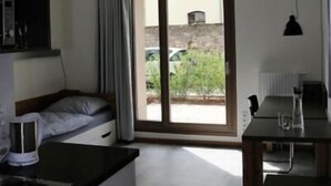 Une cuisine compacte avec un coin repas, un petit lit et une porte-fenêtre coulissante donnant sur une cour.