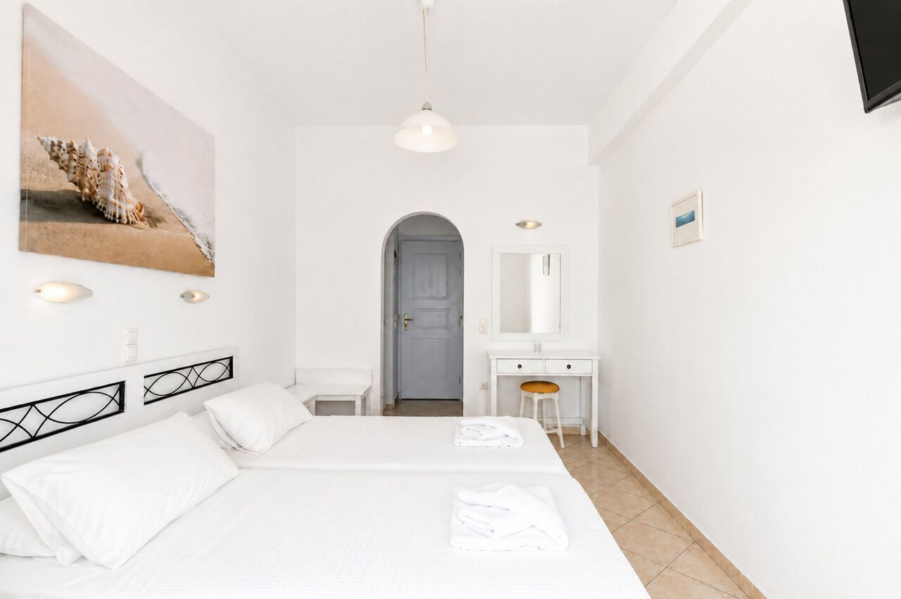 A hotel room with a bed, a desk, a chair, a mirror, and a painting on the wall.