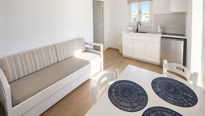 A modern living room with a sofa, a dining table with placemats, and a kitchen area with cabinets and a sink. - Eleftheria Hotel (Mykonos)