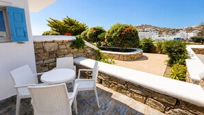 A patio with white wicker furniture, a stone wall, and a view of the sea and buildings in the background. - Eleftheria Hotel (Mykonos)