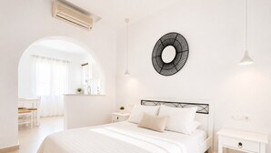 A bedroom with a bed, bedside tables, a wall-mounted mirror, and a pendant light. - Eleftheria Hotel (Mykonos)