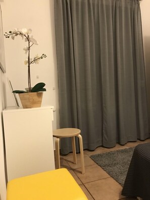 A small, compact room with a single bed, a small table, a potted plant, and a grey curtain.