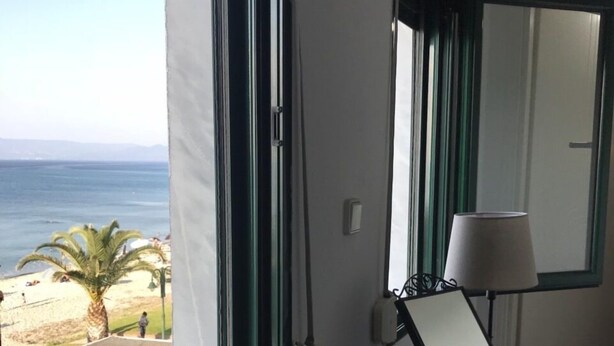 A room with a large window offering a view of the beach and ocean. There is a desk with a lamp and a magazine on it. - Stunning sea-front maisonette (Kassandra)