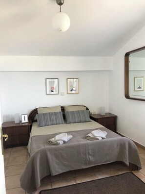 A bedroom with a bed, bedside tables, a mirror, and framed pictures on the wall. - Stunning sea-front maisonette (Kassandra)