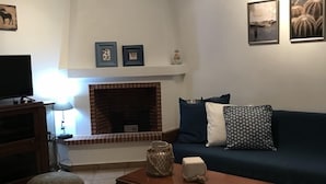 A living room with a fireplace, a sofa, a coffee table, and a television. - Stunning sea-front maisonette (Kassandra)