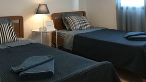 A room with two beds, a nightstand with a lamp, and a window with curtains. - Stunning sea-front maisonette (Kassandra)
