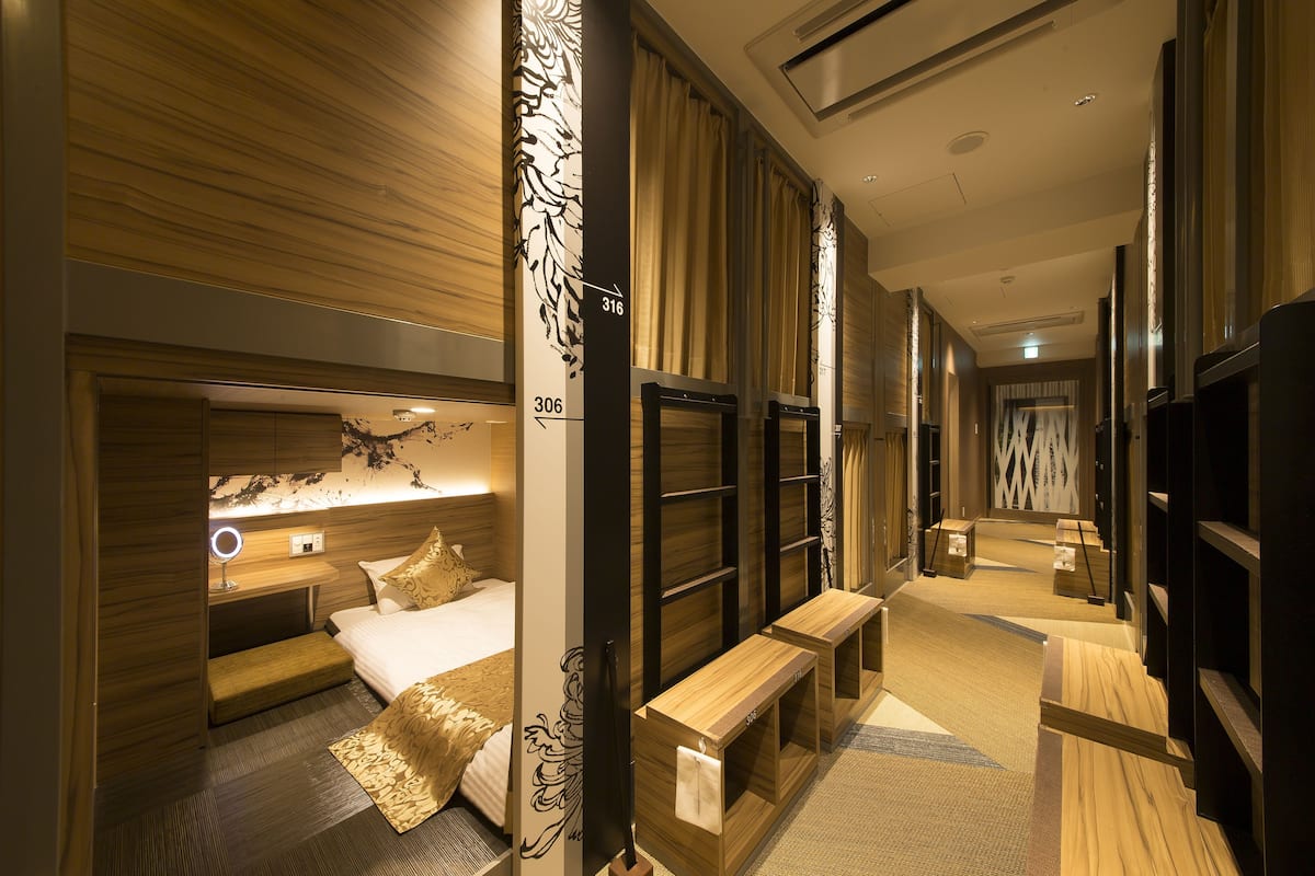 A hotel room with a bed, bedside table, mirror, and a bench.