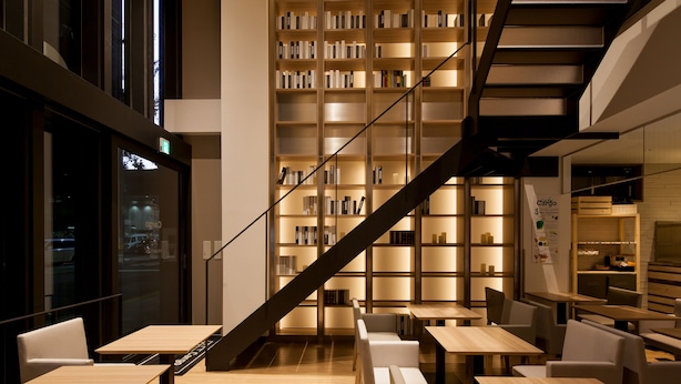 A modern library with bookshelves, a staircase, and seating areas. - HOTEL Cargo Shinsaibashi (Osaka)