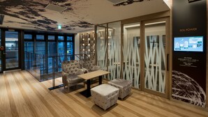 A modern interior with a wooden floor, a tufted armchair, a small table, and a sofa. There is a glass partition with a view of the outside. - HOTEL Cargo Shinsaibashi (Osaka)