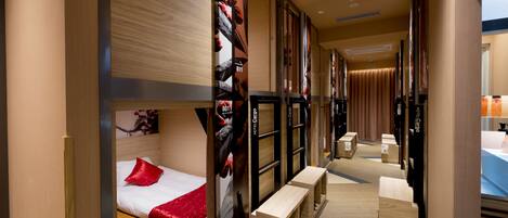 A hotel room with a bed, a red throw pillow, a wooden headboard, a mirror, and a luggage storage area.