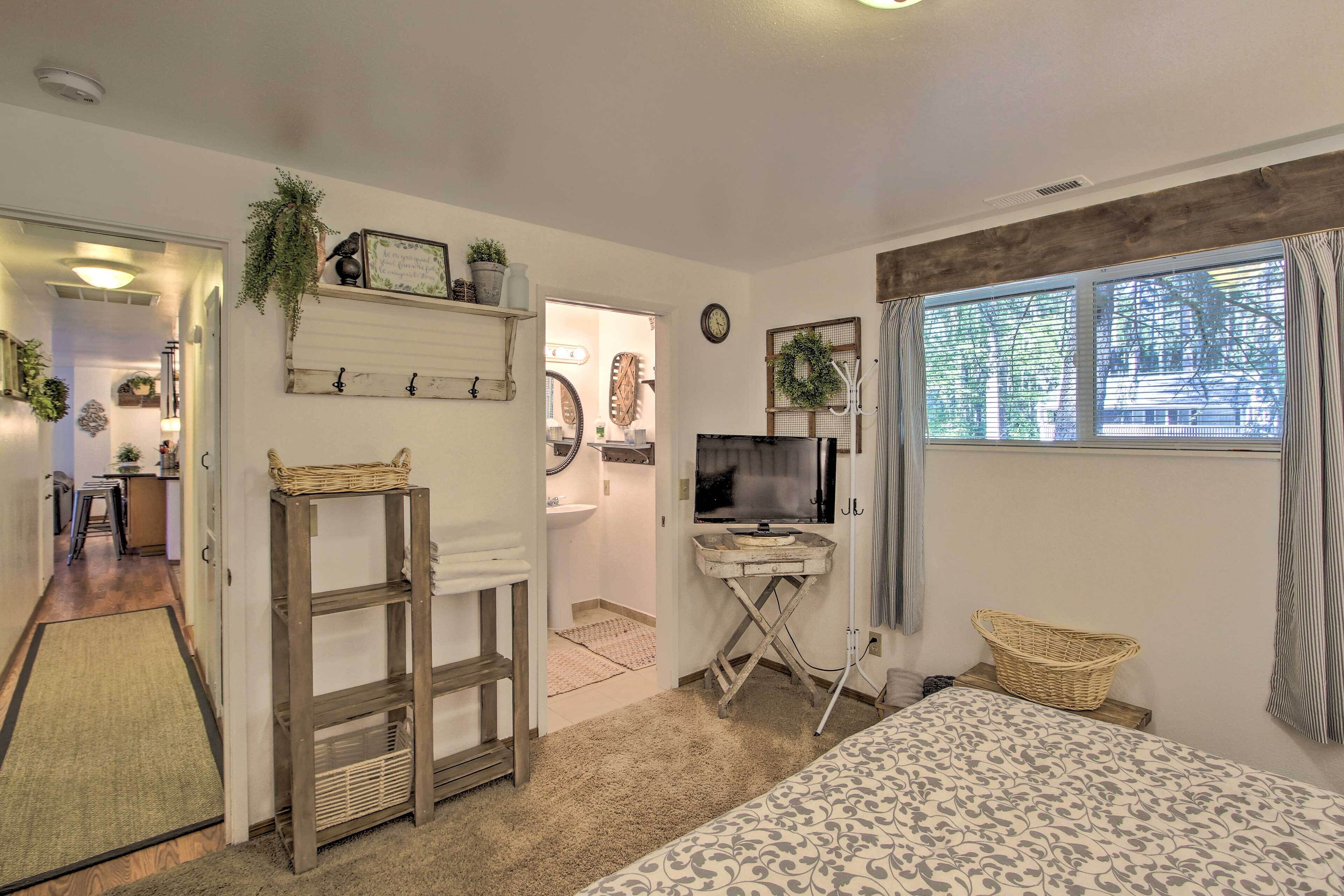 A cozy bedroom with a bed, a TV, a desk, and a window with curtains.