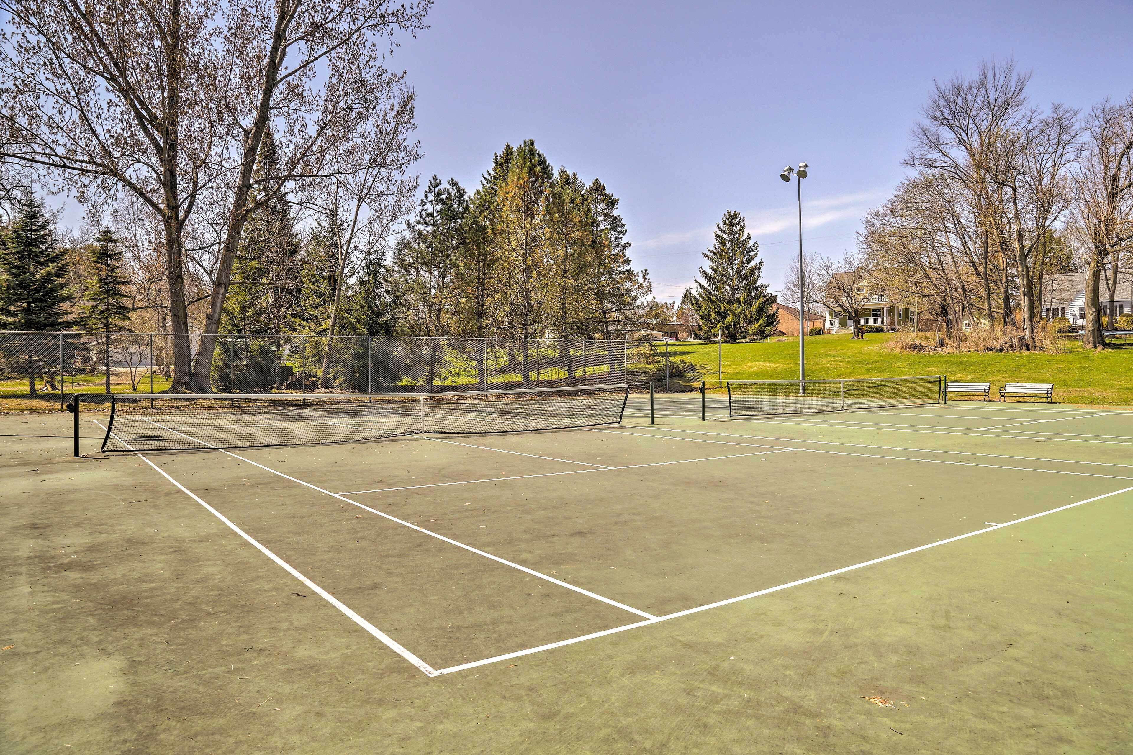 A tennis court with a net, surrounded by trees and a fence.