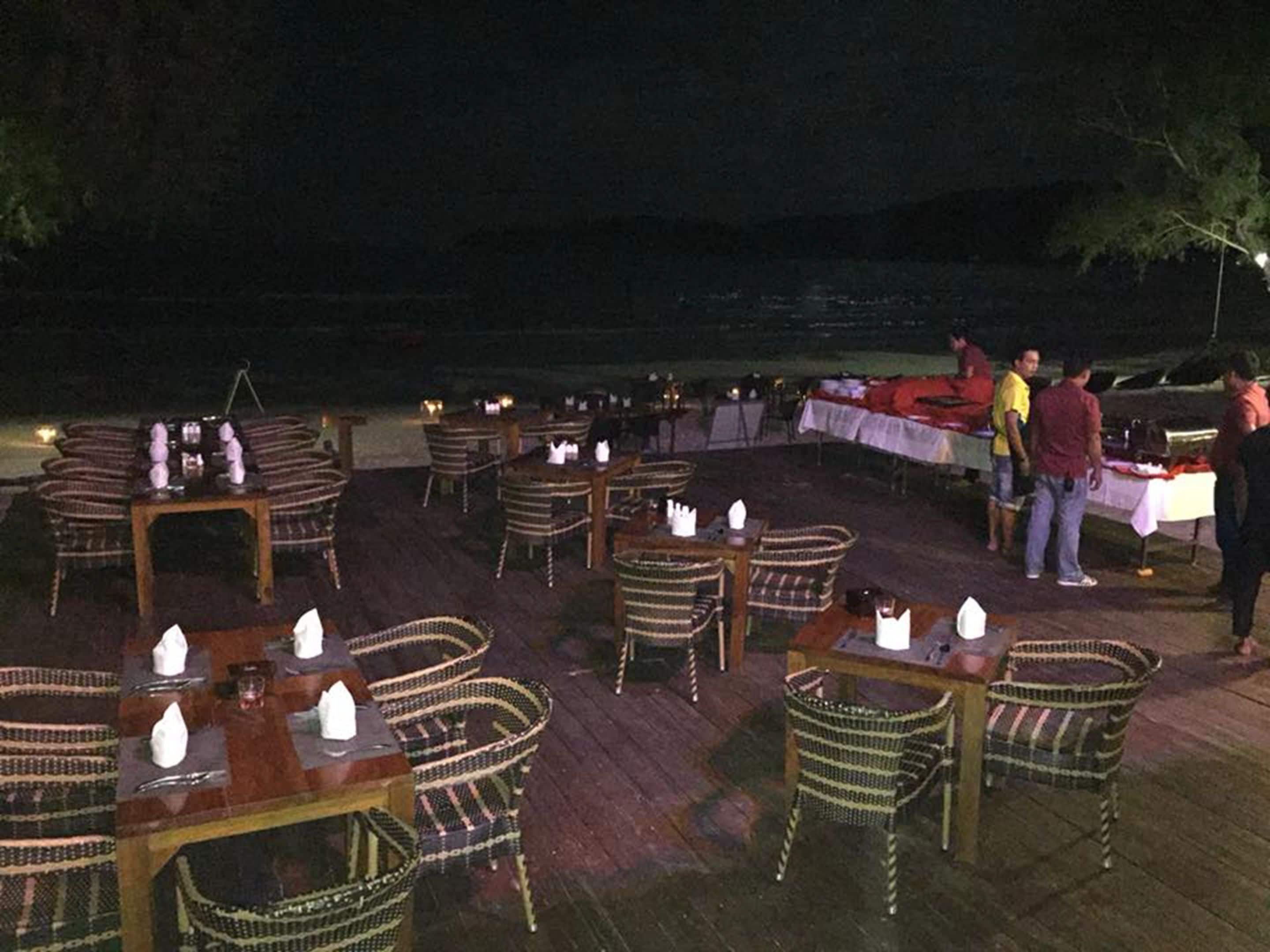 Un área de comedor al aire libre con sillas y mesas de mimbre, preparada para cenar por la noche con velas.