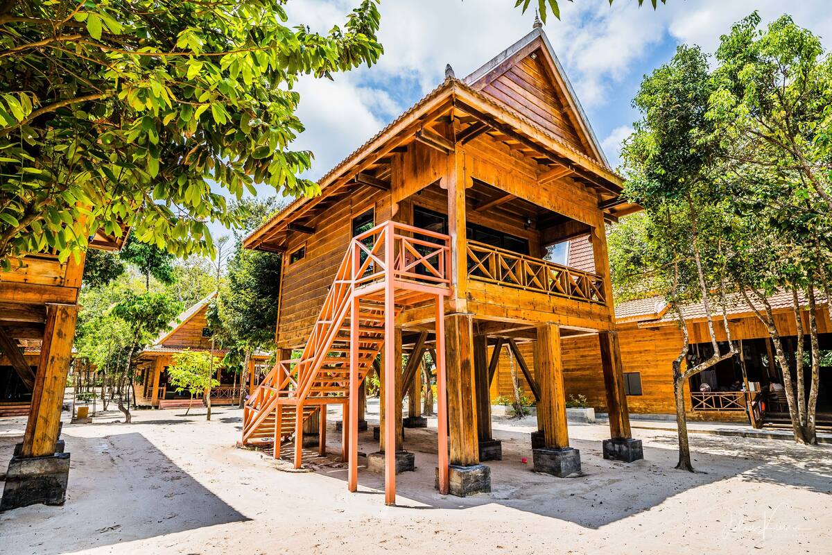 A wooden cabin with a staircase leading to the entrance, surrounded by trees and a clear sky.