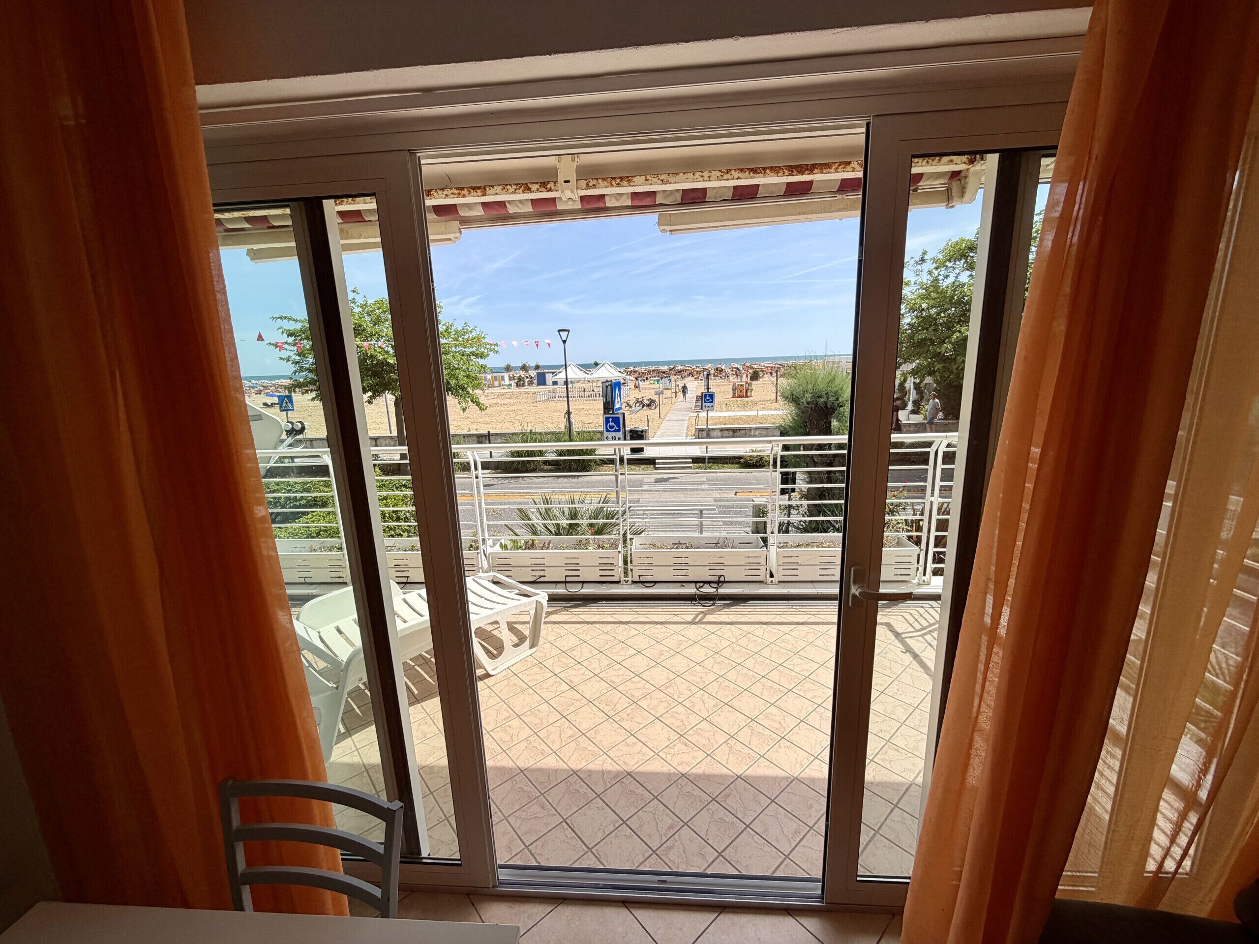 A balcony with a view of a beach, outdoor seating, and a railing.