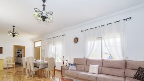 Een ruime woonkamer met een beige bank, een glazen salontafel, en een eethoek met een tafel en stoelen.