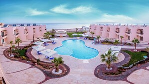 Un resort con piscina central, palmeras y vista al mar.