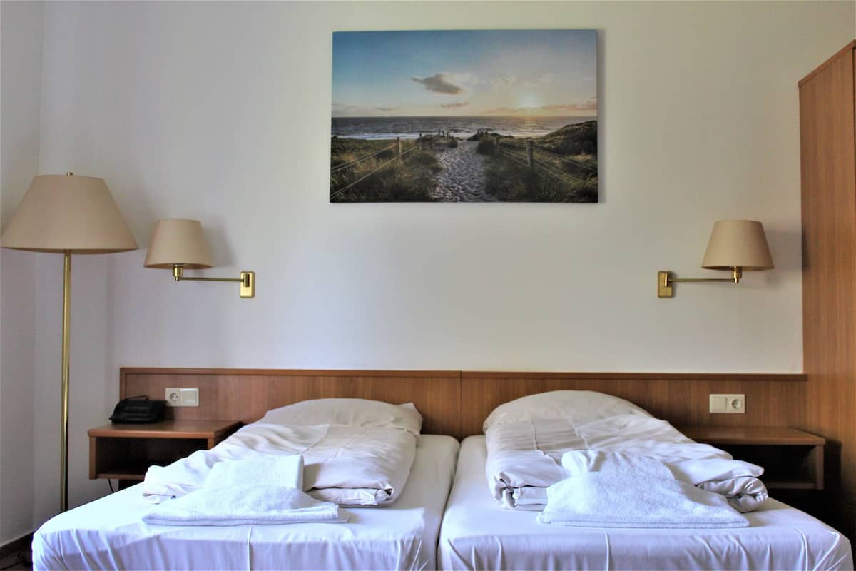 A hotel room with two beds, a painting of a beach scene, and two bedside lamps.