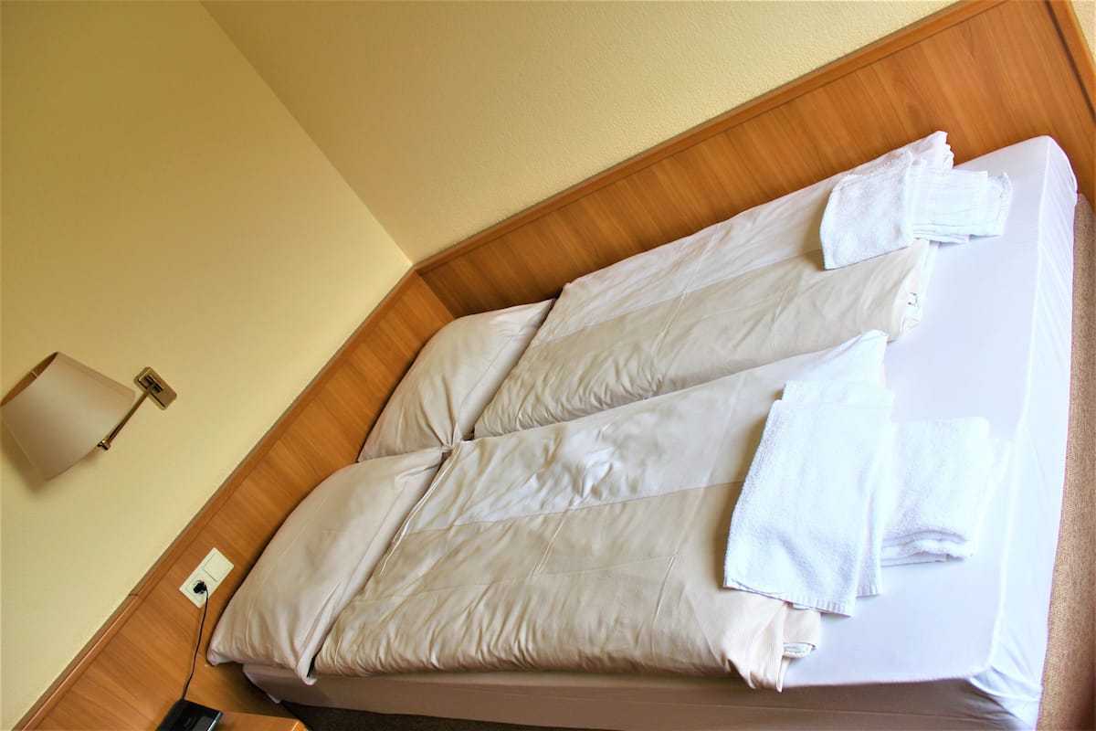 A neatly made bed with white linens and towels, a wooden headboard, and a wall-mounted lamp.