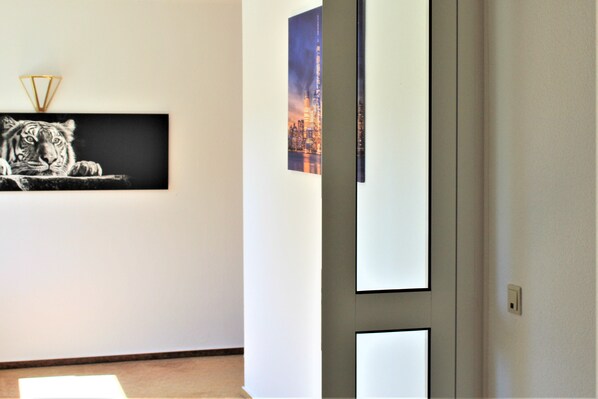 A hallway with a framed tiger picture on the left, a cityscape on the right, and a door with a light switch.