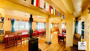 A spacious inn with wooden floors and tables, a central pillar, and a view of the outdoors. Flags are hung on the ceiling, and there are signs for guest books and games.