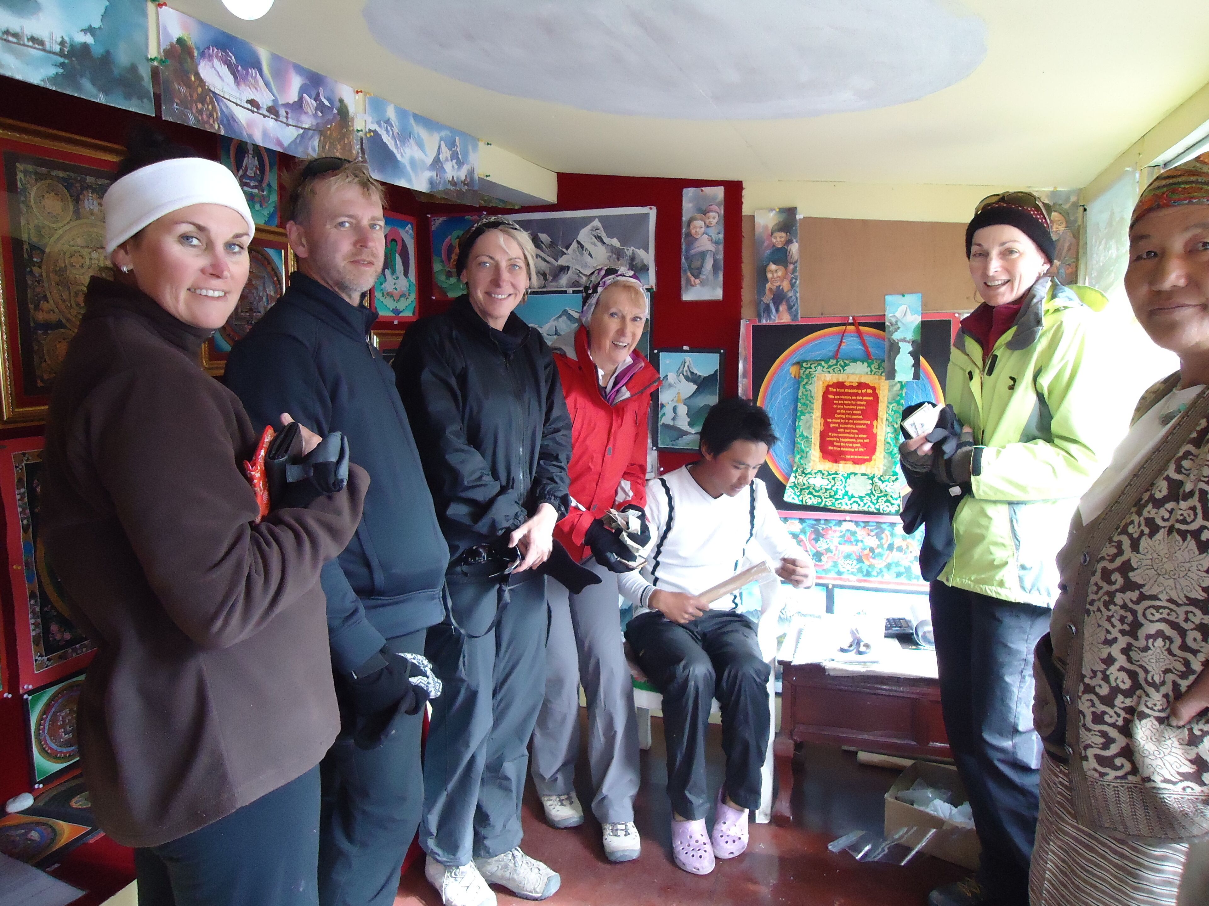 Un grupo de personas en una habitación con varias obras de arte en las paredes, un banco y una mesa con un objeto decorativo.