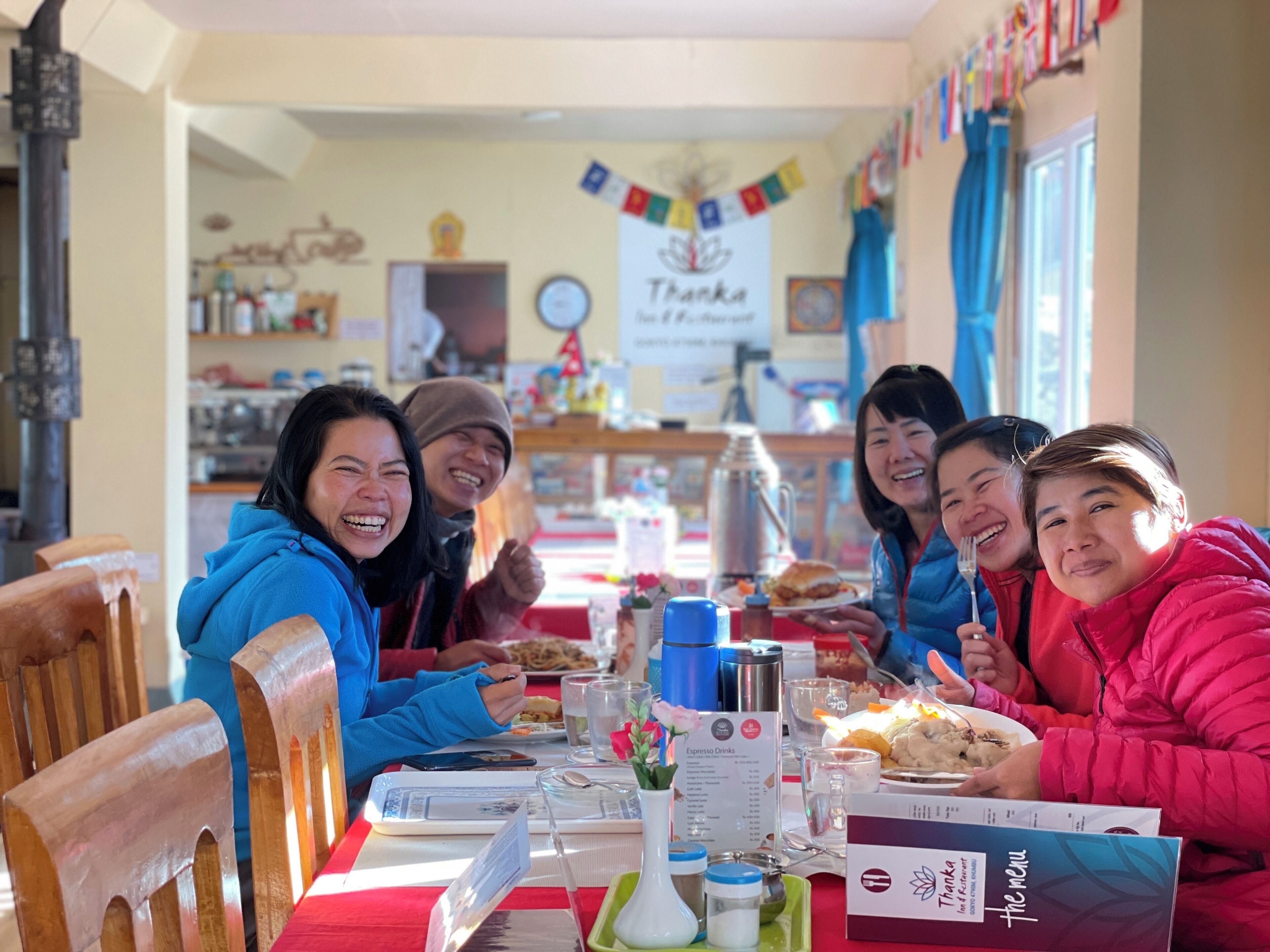 A group of people dining at a restaurant with a red tablecloth, menu, and various dishes.