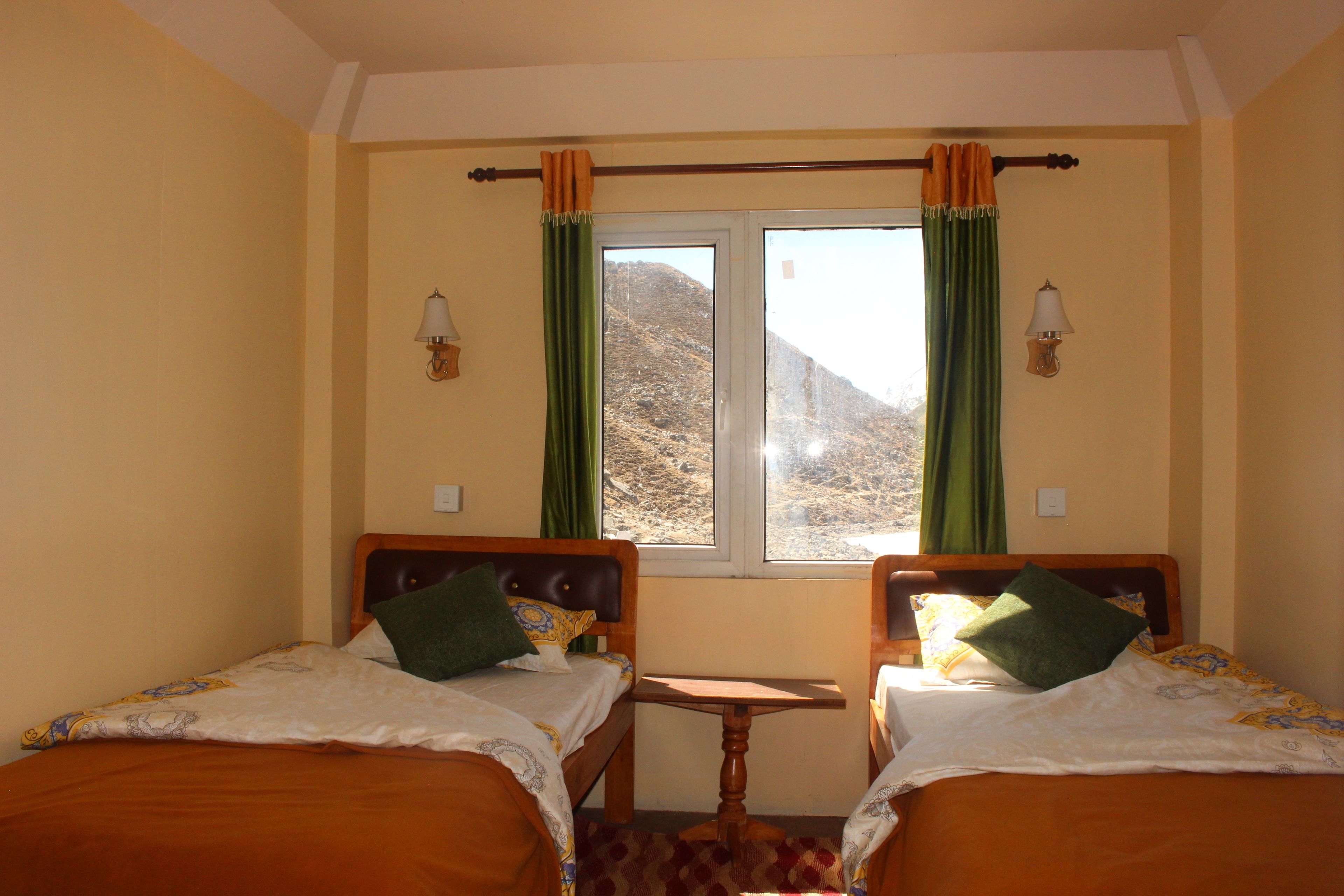 Une chambre avec deux lits, une petite table et une fenêtre avec des rideaux.