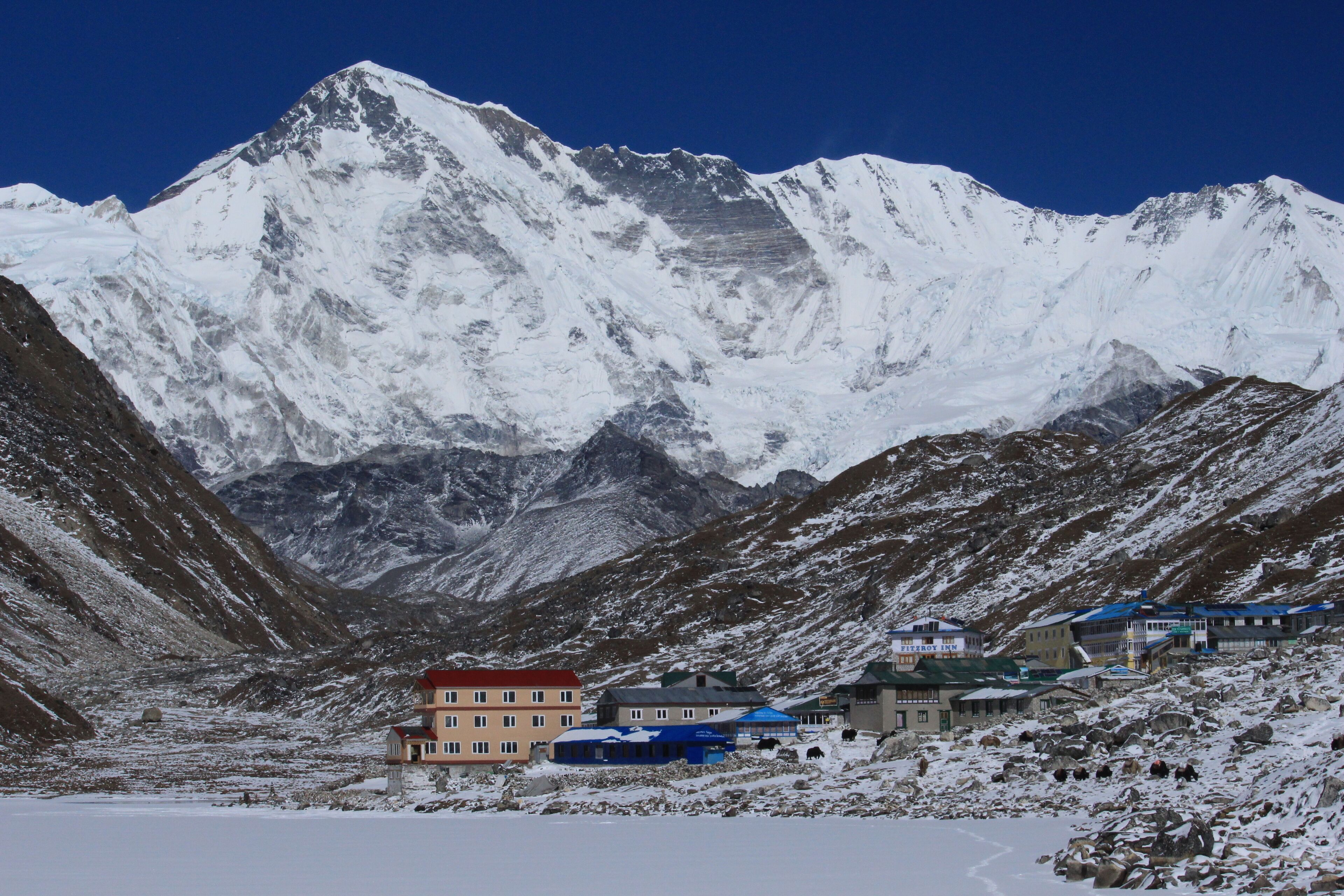 A mountainous area with a snow-covered peak and several buildings with red and blue roofs.