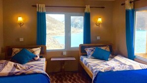 Una habitación con dos camas, cada una con cubrecama y almohadas azules, una mesita y dos lámparas fijadas a la pared.