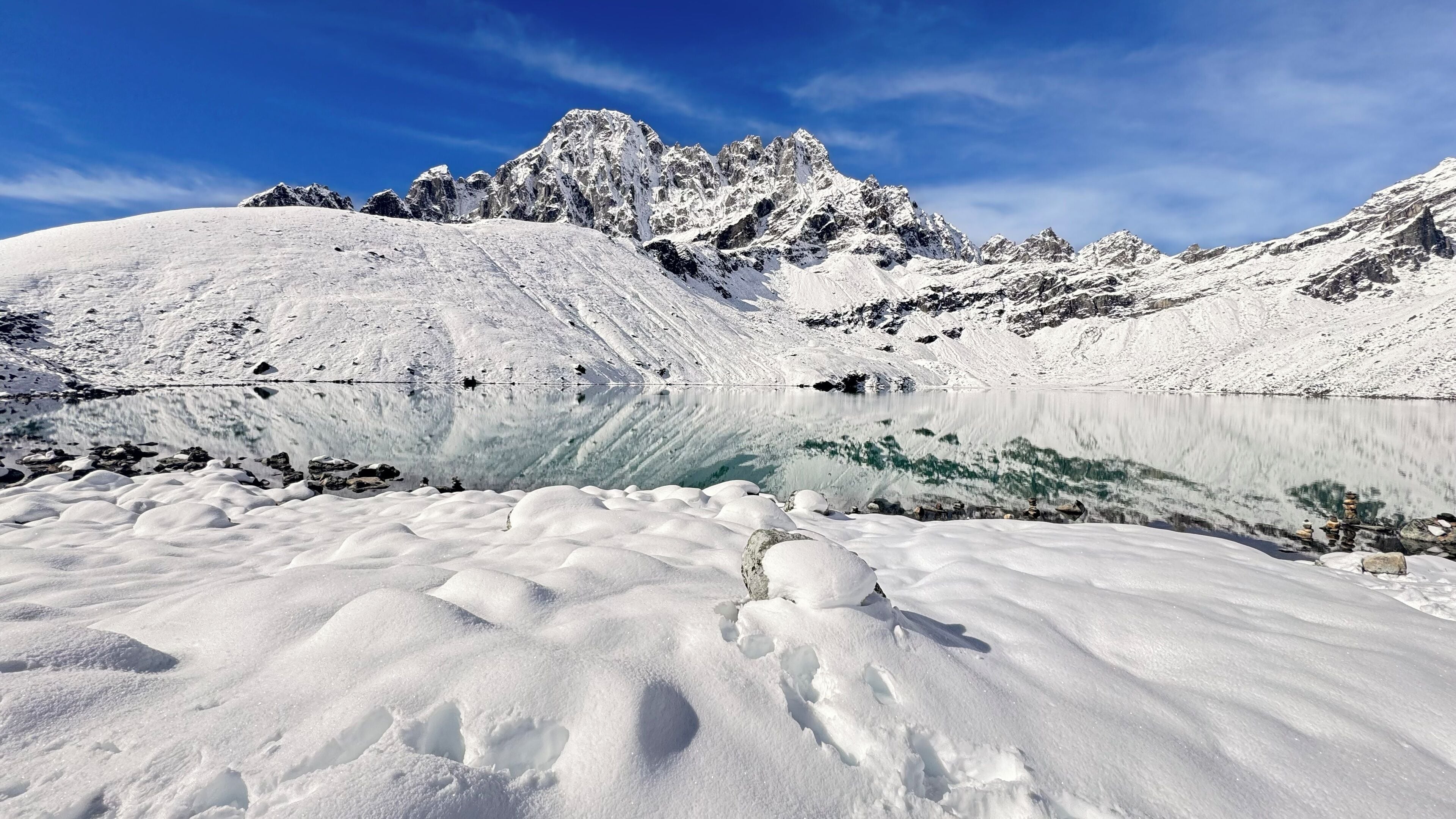A snow-covered mountain range with a clear lake in the foreground.