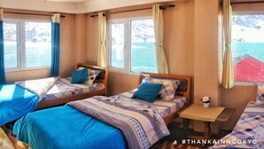 Una habitación con dos camas, una mesita pequeña y ventanas grandes con vistas al mar.
