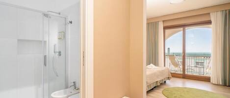 A hotel room with a balcony, a shower, a toilet, and a bed.