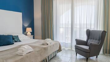 Ein Hotelzimmer mit einem Bett, einem Sessel, einem Nachttisch mit Lampe und einem Fenster mit Vorhängen.