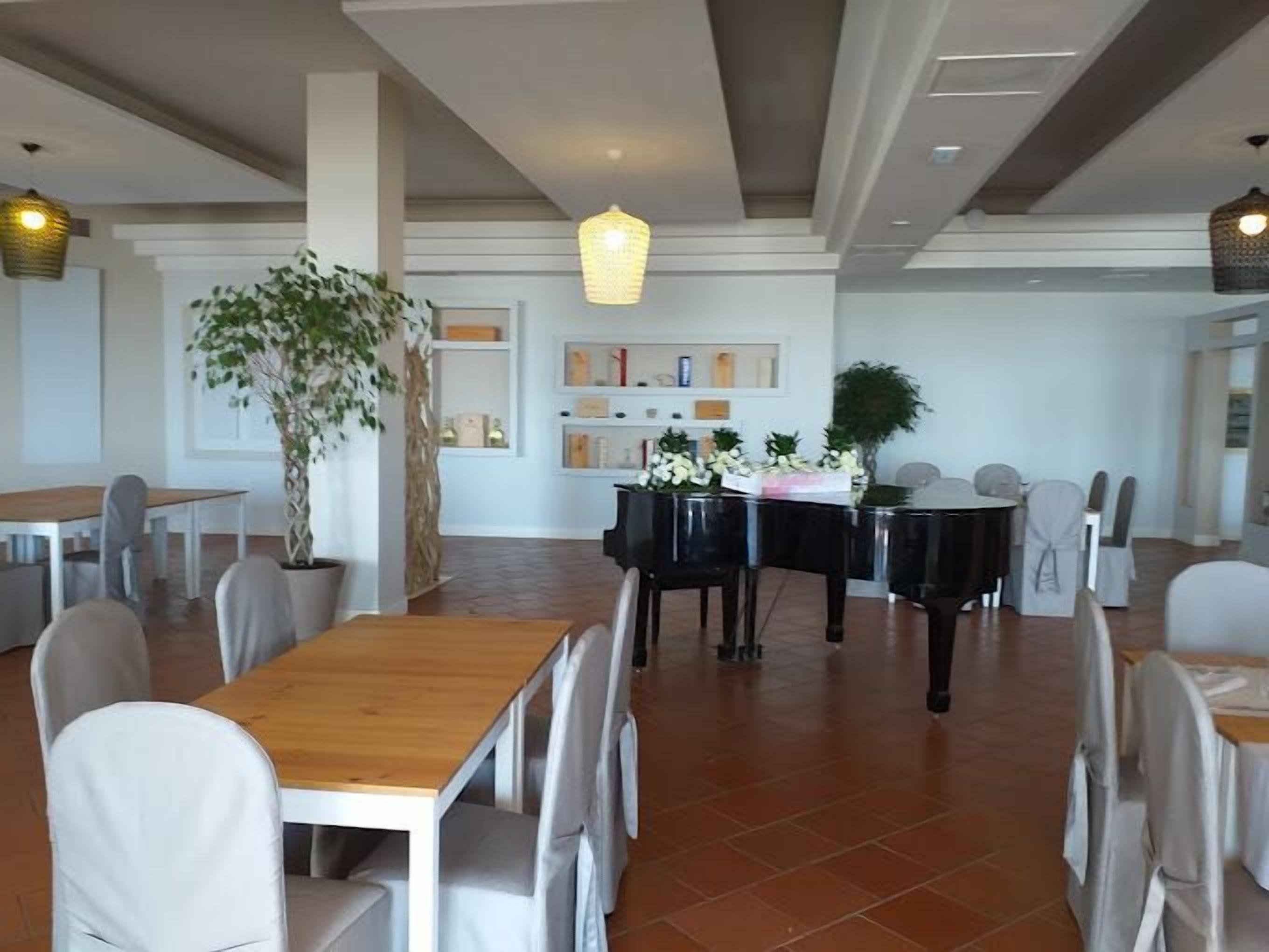 A spacious dining area with multiple tables and chairs, a piano, and decorative plants.