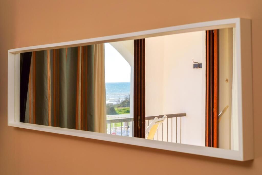 Ein Zimmer mit einem großen Spiegel, der einen Balkon mit Vorhängen und Meerblick zeigt.