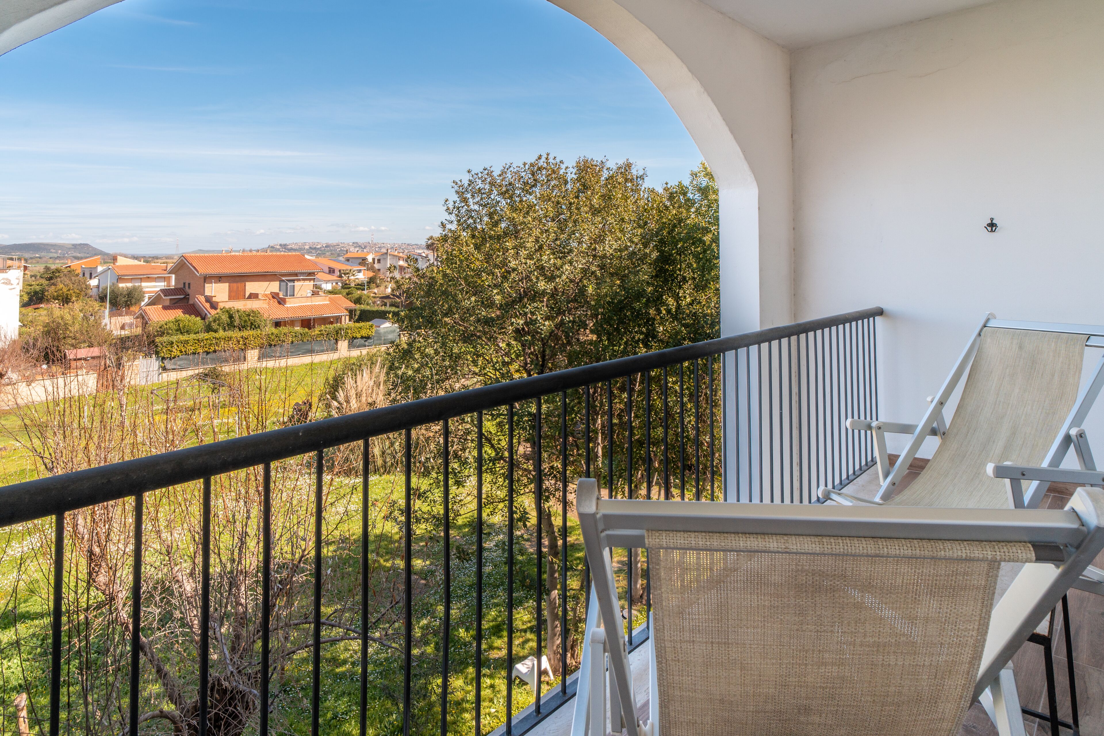 A balcony with a view of a residential area, a chair, and a railing.