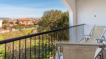 A balcony with a view of a residential area, a chair, and a railing.