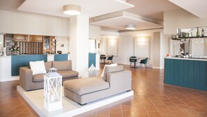 A modern living room with a sofa, a coffee table, and a decorative lantern. There is a kitchen area with a bar and a dining table with chairs. - Smy Civico Zero (Tarquinia)