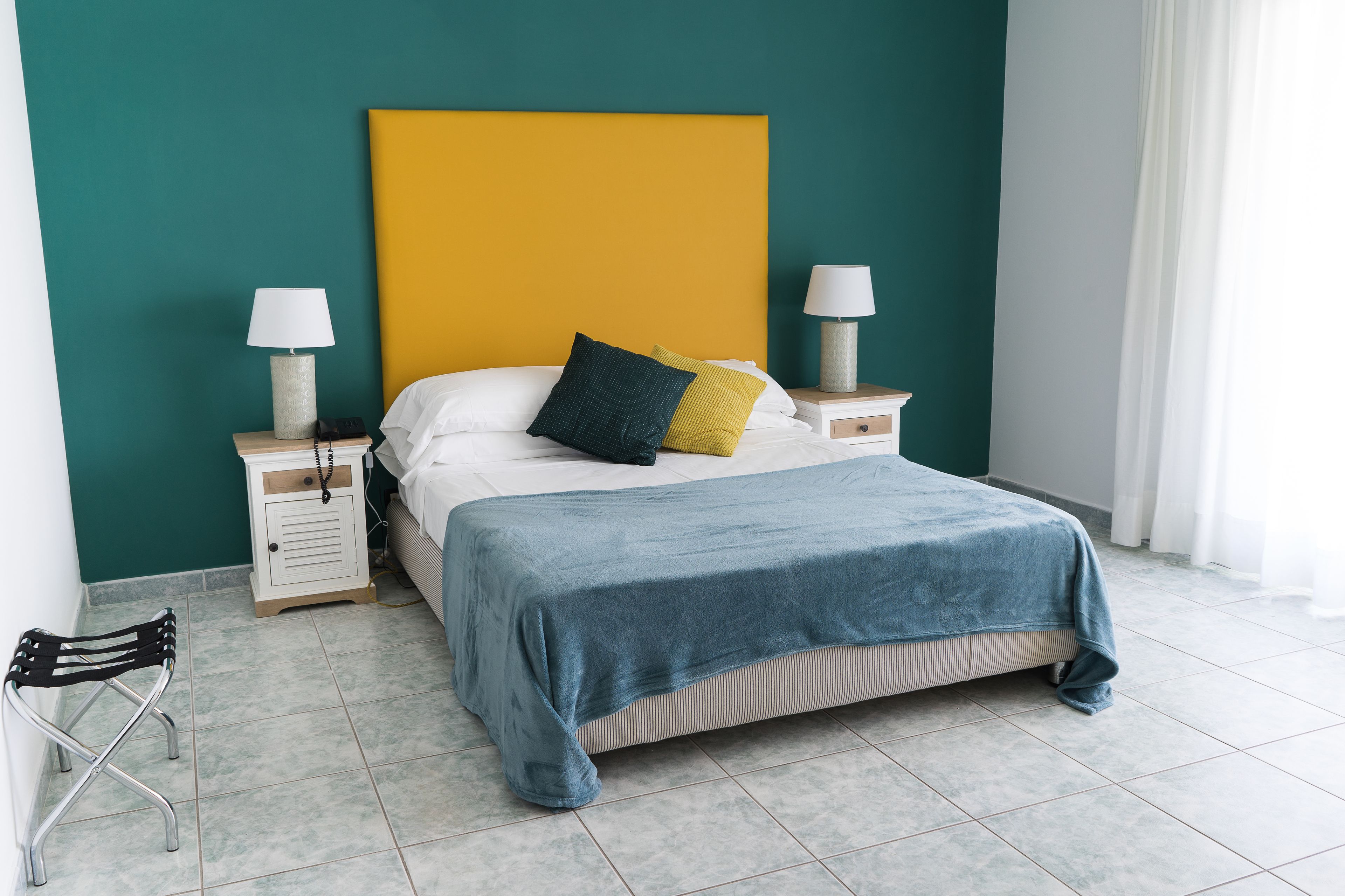 Una cama bien hecha con un edredón azul, dos lámparas de noche y una mesita de noche con lámpara.