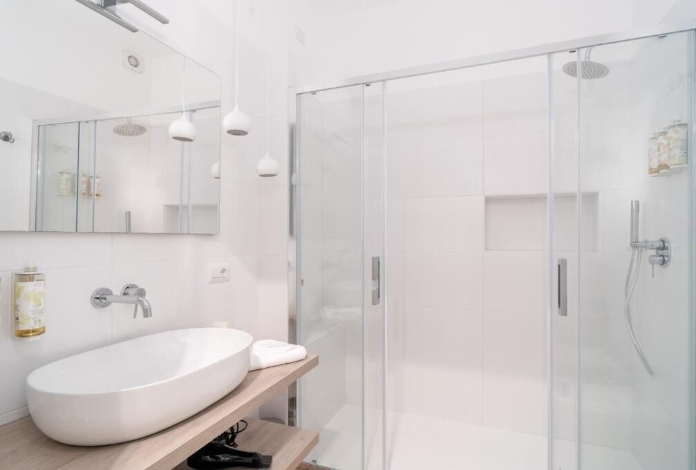 A modern bathroom with a large oval sink, a glass shower enclosure, and a wooden shelf.