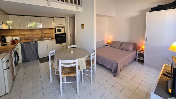 A compact, modern apartment with a kitchenette, a dining area, and a bedroom.