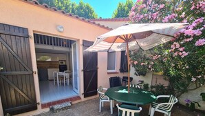 A patio with a table and chairs, a covered umbrella, and a view of a house with a garage door.