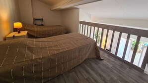 A balcony with two beds, a nightstand with a lamp, and a view of the outside.
