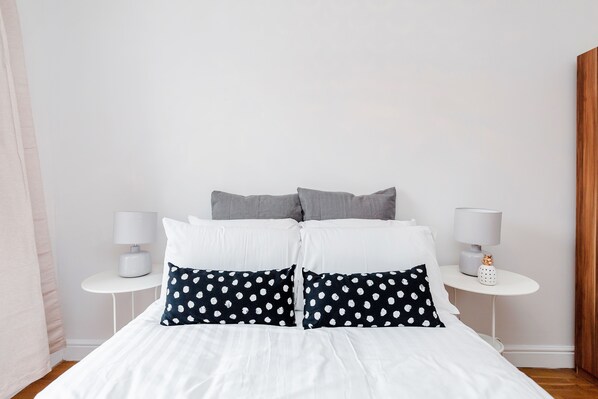 A neatly made bed with white and navy pillows, two bedside tables with lamps, and a wooden door.