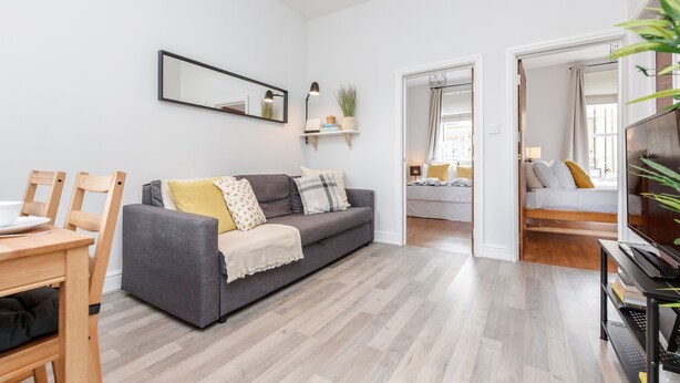 A modern living room with a grey sofa, wooden floor, and a dining area with a table and chairs. - WelcomeStay Clapham Junction 2 bedroom Apartment (London)