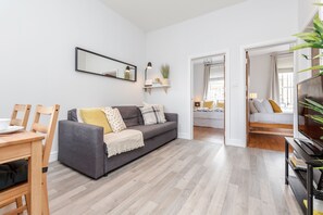 A modern living room with a grey sofa, wooden floor, and a dining area with a table and chairs.
