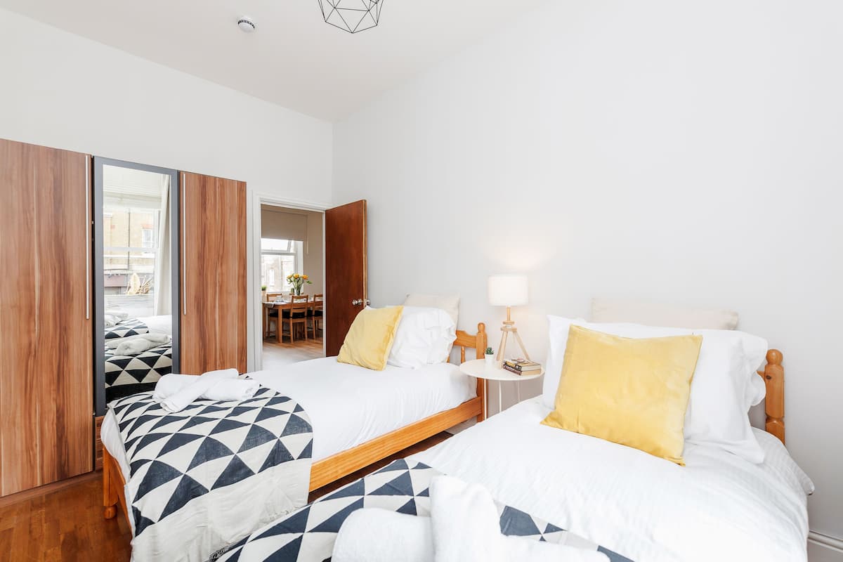 Een hotelkamer met twee bedden, houten vloeren, een tafeltje met een lamp en uitzicht op buiten.